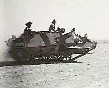 A tracked military vehicle moves across the desert