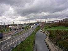 View from a bridge over a canal, with a motorway running to the left. The sky is dark and overcast.