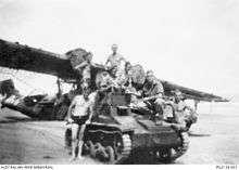 Soldiers sitting on a small armoured vehicle in front of a grounded aircraft