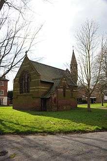 A photograph of a brown building with a sloped roof and a tower protruding from the right portion of the roof all surrounded by green grass