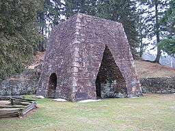 A large stone iron furnace with openings on each of the two sides visible