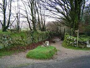 An earthen lane circles a raised grassy area containing a large stone