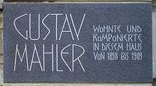 A dark plaque with white lettering in which the composer's name is shown in extra large characters on the left, the main message in smaller characters on the right