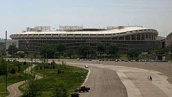 A large circular stadium with a curving overhang behind a mostly unused parking lot.