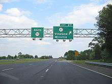 A four lane freeway at an interchange. Two green overhead signs stand over the road with the left one reading south Route&nbsp;55 and the right one reading exit&nbsp;27 Route&nbsp;47 Vineland Millville with an arrow pointing to the upper right