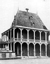 Large two-storey wood building with decoratively carved verandas supported by tall pillars
