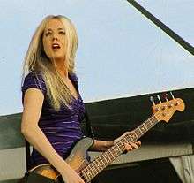 A 32-year-old woman is playing a four-string electric bass guitar.