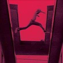 A red-tinted film still showing a boy jumping from one roof to another