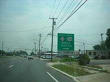 A four lane undivided road in a business area approaching a traffic light. A sign on the right side of the road reads south Route&nbsp;54 north U.S. Route&nbsp;206 Buena Trenton right all turns right